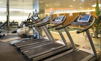 a modern gym with multiple treadmills and exercise equipment , including a pool area visible through the windows at Garden City Hotel