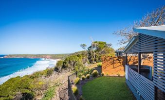 a house is situated on a hillside overlooking the ocean , with a fence in front of it at NRMA Merimbula Beach Holiday Resort