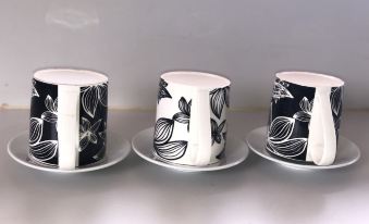 three black and white cups with floral designs are lined up on a white plate at EastWest Hospitality