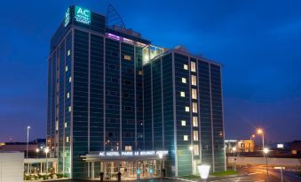 "a large hotel with a sign that says "" ac hotel grand marina grand "" is illuminated at night" at AC Hotel Paris le Bourget Airport