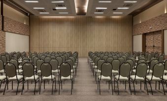 an empty conference room with rows of black and white chairs , a wooden wall , and ceiling lights at Tivoli Ecoresort Praia do Forte