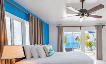 a bedroom with a bed , white linens , and a fan next to a sliding glass door leading to a balcony overlooking the ocean at Pelican Beach Hotel
