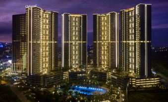 a tall building with multiple levels and large windows is illuminated at night , surrounded by water at Oakwood Apartments Pik Jakarta