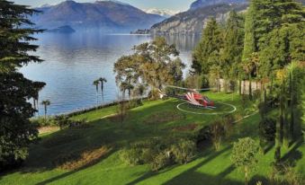 a serene landscape with a lake , mountains , and green grass , featuring a helicopter flying over the water at Villa Lario Resort Mandello