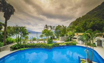 a large , blue swimming pool surrounded by lush greenery and mountains , with a view of the ocean in the distance at Hotel la Riviera de Atitlán