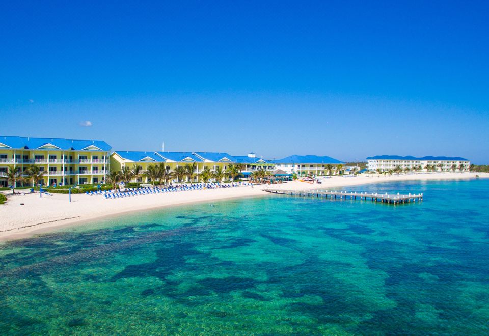 a beautiful beach with clear blue water and white sand , surrounded by buildings and palm trees at Wyndham Reef Resort Grand Cayman