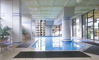 an indoor swimming pool with a blue and white color scheme , surrounded by tall windows and a building in the background at Milson Serviced Apartments