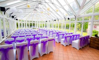 a large white room with tables and chairs covered in purple tablecloths , surrounded by windows at Kincaid House Hotel