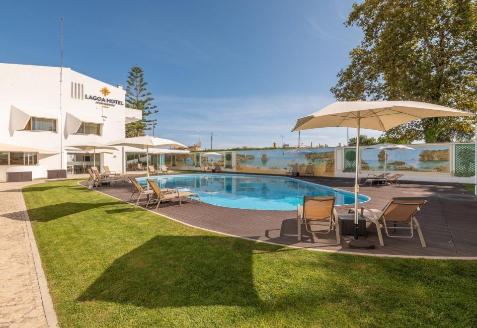 a large swimming pool is surrounded by lounge chairs and umbrellas , with a building in the background at Lagoa Hotel