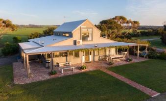 a large wooden house with a porch and patio , surrounded by green grass and trees at Bear Gully Coastal Cottages