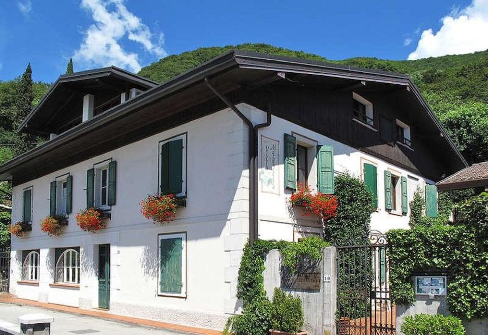 a white and green building with flower pots on the windows , set against a backdrop of mountains and blue sky at Villa Margherita