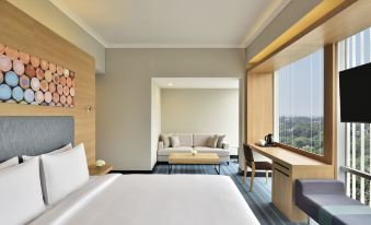 a modern hotel room with a large window offering a view of the city , white bed , and wooden furniture at Aloft New Delhi Aerocity