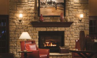 a cozy living room with a fireplace , two red chairs , and a painting on the wall at DoubleTree by Hilton Hotel Cincinnati Airport