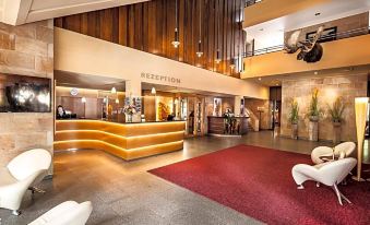 a modern hotel lobby with a reception desk , seating area , and large windows , decorated with red rugs and wooden paneling at Berghotel Bastei