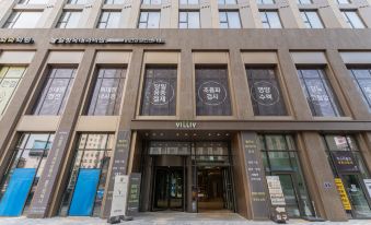 The front entrance of a hotel features a glass and steel design with an oriental-style sign above it at HOMES Stay Myeongdong