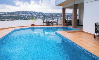 a large swimming pool with a wooden deck and chairs on the side , overlooking a city skyline at Gold Crest Hotel