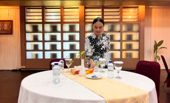 a woman in a black and white floral dress is setting up a table with various items on it , including water bottles , cups , and a at Asana Biak Papua Hotel