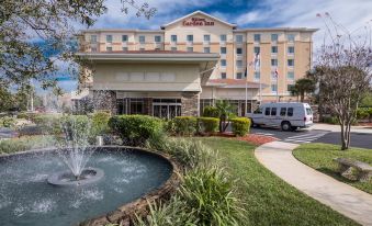 a large hotel with a fountain in front of it , surrounded by green grass and trees at Hilton Garden Inn Tampa/Riverview/Brandon