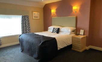 a large bed with a black and white comforter is in a bedroom with a window , nightstands , and wall lights at The Windmill Inn