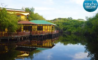 a yellow wooden house on stilts over a body of water , surrounded by lush greenery at Hotel Estero y Mar