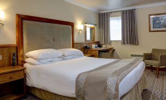 a large bed with white sheets and a beige headboard is in a room with a window at Best Western Plus Pastures Hotel