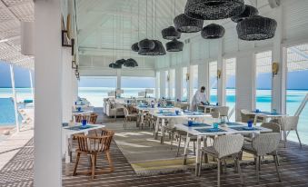 a restaurant with white tables and chairs , blue tablecloths , and black pendants hanging from the ceiling at Four Seasons Resort Maldives at Landaa Giraavaru