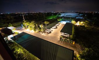 an aerial view of a parking lot at night , with several cars parked and buildings in the background at The Living Hotel SamutPrakan