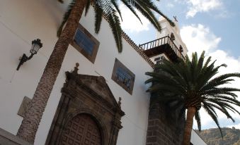 a white building with palm trees in front of it , and a doorway with palm trees on either side at Hotel San Roque