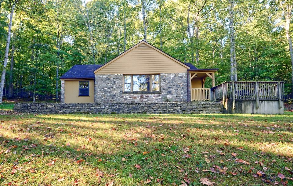 a small stone house surrounded by trees and grass , with a wooden deck in front of it at Carter Caves State Resort Park