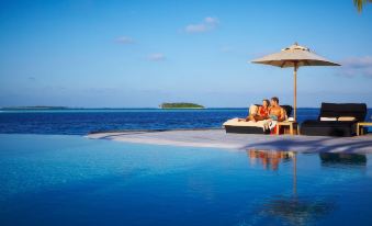 a man and a woman are sitting on a lounge chair by the ocean , enjoying the view at Komandoo Island Resort & Spa