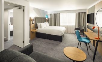 a modern hotel room with a large bed , gray carpeting , and a blue chair near the window at Holiday Inn Aylesbury