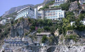 a large white building on a cliff overlooking the ocean , with boats docked in the water below at Hotel Miramalfi