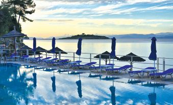 a beautiful poolside scene with umbrellas , sun loungers , and a calm blue water reflecting the sunset at Agali Hotel Paxos
