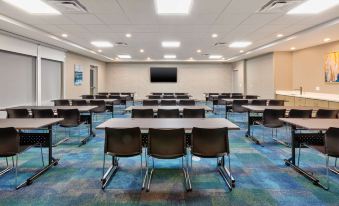 a large conference room with multiple tables and chairs , a television screen , and a blue and green patterned carpet at Home2 Suites by Hilton Battle Creek