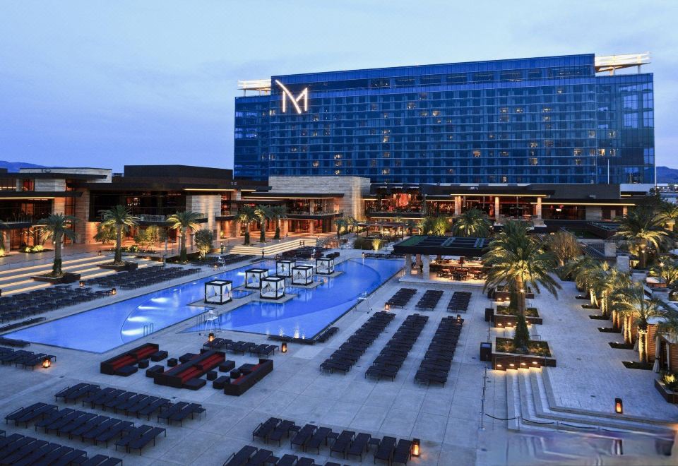a large hotel with a pool and a smaller building in the background , surrounded by lounge chairs and umbrellas at M Resort Spa & Casino