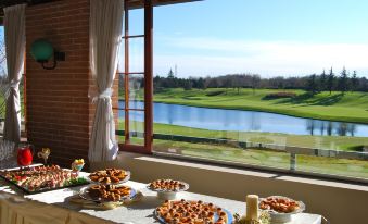 a table with a variety of food items is set up near a window overlooking a golf course at Doubletree by Hilton Milan Malpensa Solbiate Olona