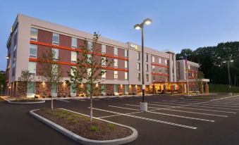 a modern building with a parking lot in front , trees , and lights on the ground at Home2 Suites by Hilton Pittsburgh/McCandless