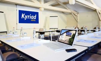 a laptop is open on a table in front of a conference room with a kyriad hotel sign at Kyriad Lille Est - Hem