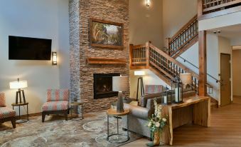 a modern living room with a fireplace , wooden stairs , and a staircase leading to the upper floor at GrandStay Hotel & Suites