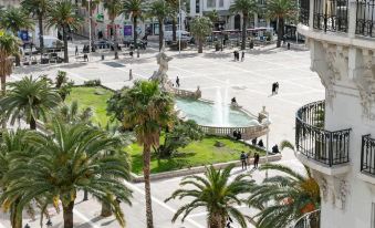 a bustling city square with palm trees , people walking around , and a fountain in the center at Okko Hotels Toulon Centre