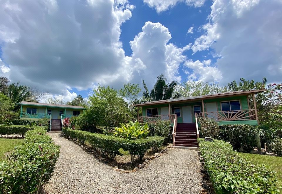 a group of three small , green houses with wooden doors and windows , surrounded by bushes and trees under a blue sky at Dream Valley Belize