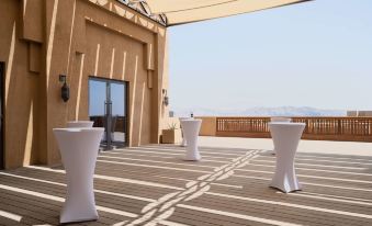 a patio area with three white tables and a beige building in the background , under a sunny sky at Anantara Al Jabal Al Akhdar Resort