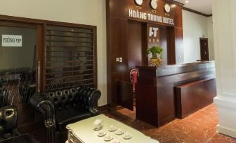 a reception area with a white desk , chairs , and a black couch in front of a brown wooden wall at Hoang Trung Hotel