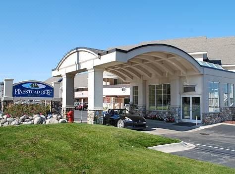 a large hotel with a parking lot in front of it , where several people are gathered at Pinestead Reef Resort