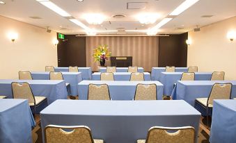 a large conference room with multiple tables and chairs , a vase of flowers , and a projector screen at Hotel Metropolitan Yamagata
