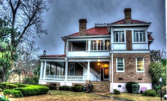 a large , two - story brick house with red tile roof and white trim , surrounded by trees and grass at 1912 Bed and Breakfast