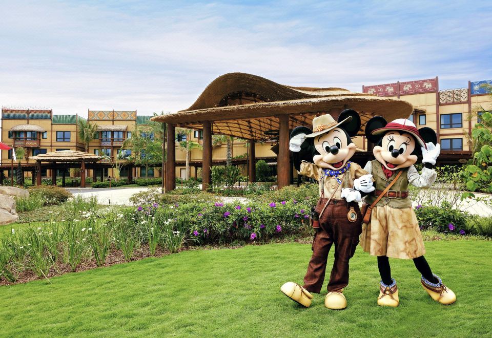 A couple stands in front of a crowd with an amusement park in the background featuring characters from various franchises at Disney Explorers Lodge