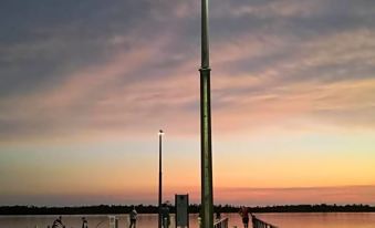 a pier with a streetlight and lampposts at sunset , reflecting the calm water below at Kalimna Woods Cottages