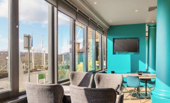 a modern living room with large windows , blue accent wall , and multiple chairs facing a television at Holiday Inn Leeds - Brighouse