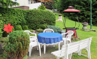 a patio set with a blue tablecloth and white chairs is surrounded by bushes and trees at Aurora